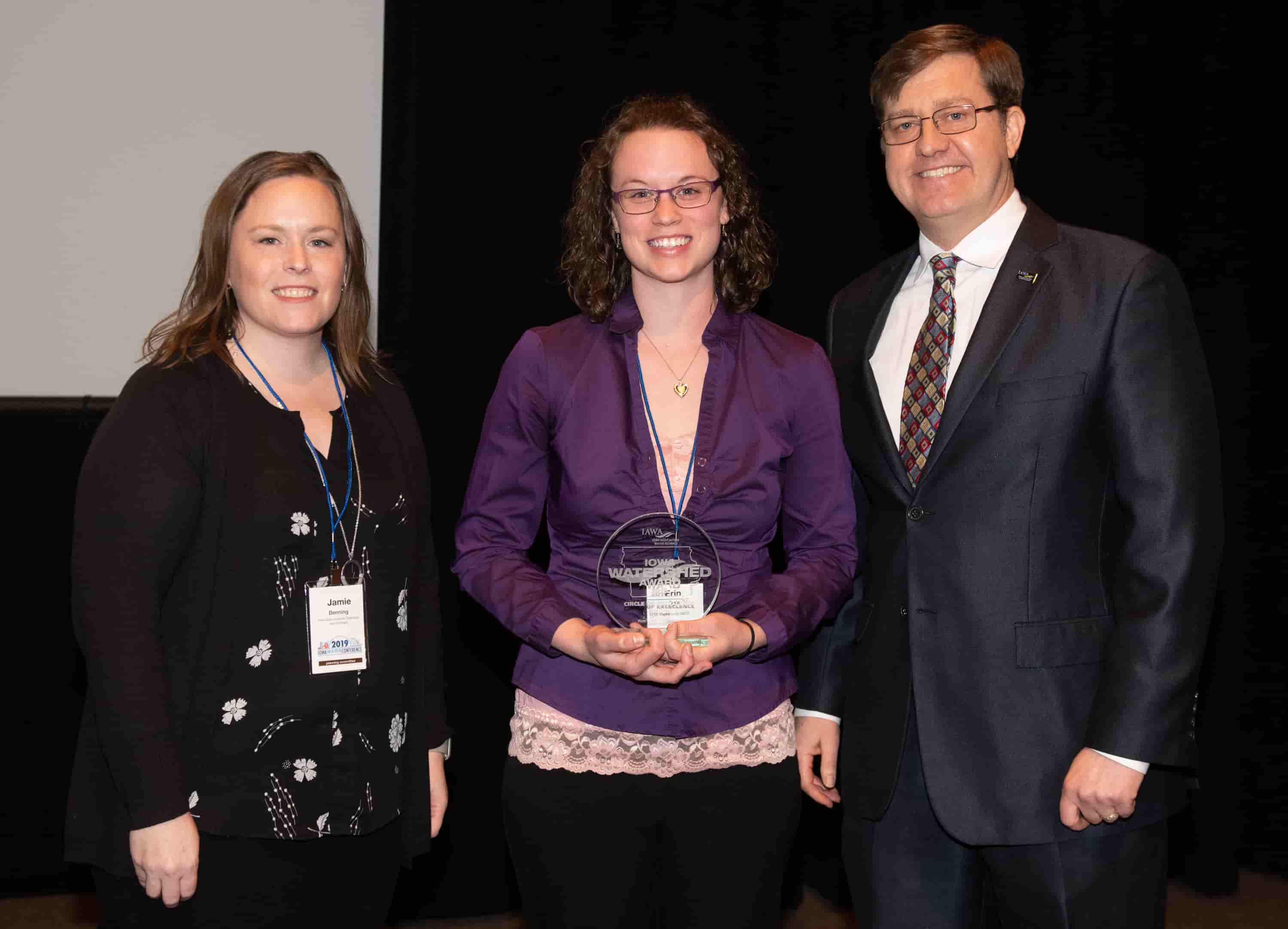 Jamie Benning with Iowa State University, Sean McMahon with Iowa Ag Water Alliance presenting Erin Ogle, watershed coordinator, with an IAWA Iowa Watershed Award